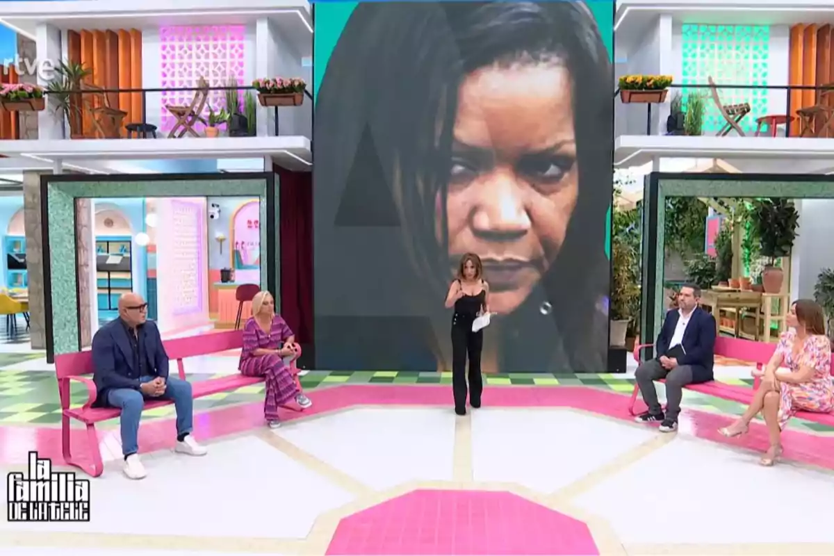 Un grupo de personas está sentado en un plató de televisión colorido, con una gran pantalla detrás mostrando el rostro de una mujer. Captura de 'La Familia de la Tele' Un grupo de personas está sentado en un plató de televisión colorido, con una gran pantalla detrás mostrando el rostro de una mujer. Captura de 'La Familia de la Tele'
