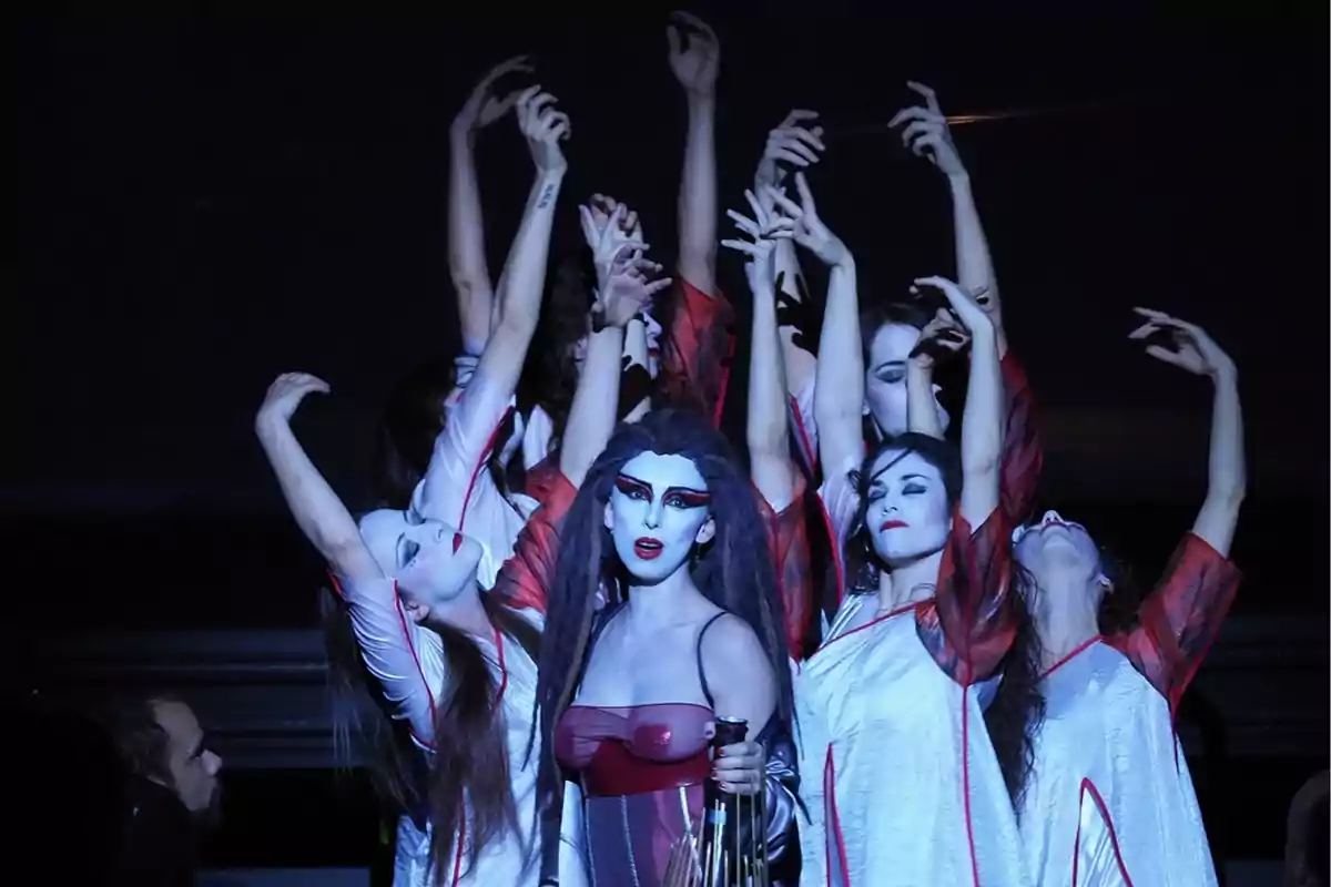 actrices de una obra de teatro vestidas de blanco y rojo sobre un escenario oscuro únicamente iluminado por un foco