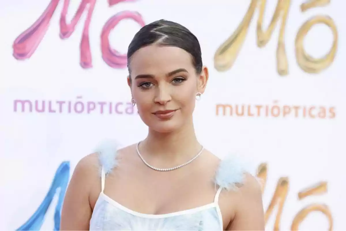 Una mujer con un vestido blanco y detalles de plumas posa frente a un fondo con el logotipo de MultiÓpticas.