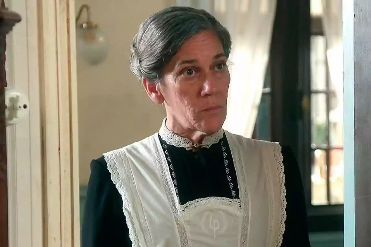 Petra con cabello canoso recogido vestida con uniforme de sirvienta antiguo en una casa elegante. Captura de 'La Promesa' Petra con cabello canoso recogido vestida con uniforme de sirvienta antiguo en una casa elegante. Captura de 'La Promesa'