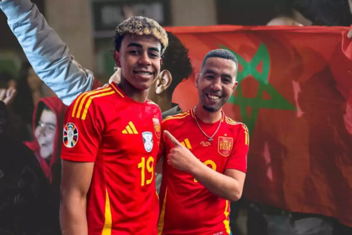 Dos personas con camisetas rojas de la selección española de fútbol posan sonriendo frente a una bandera de Marruecos.