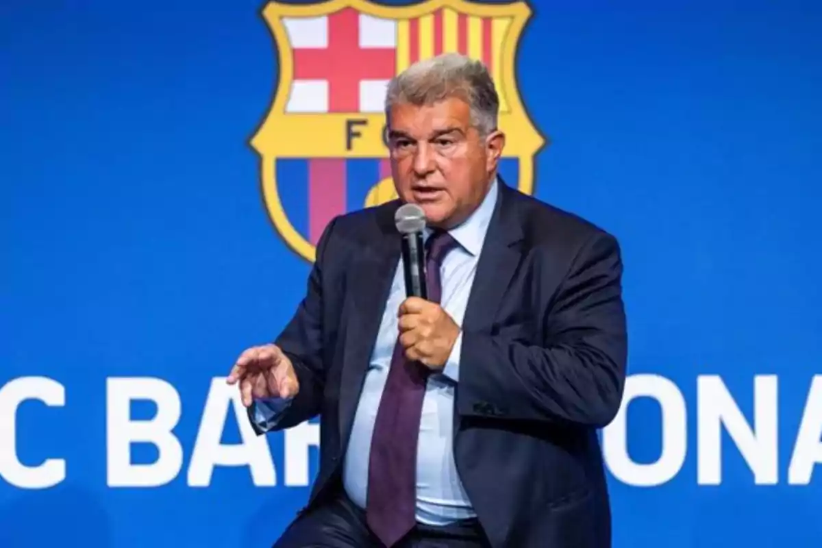 Hombre en traje hablando con un micrófono frente a un fondo azul con el escudo del FC Barcelona.