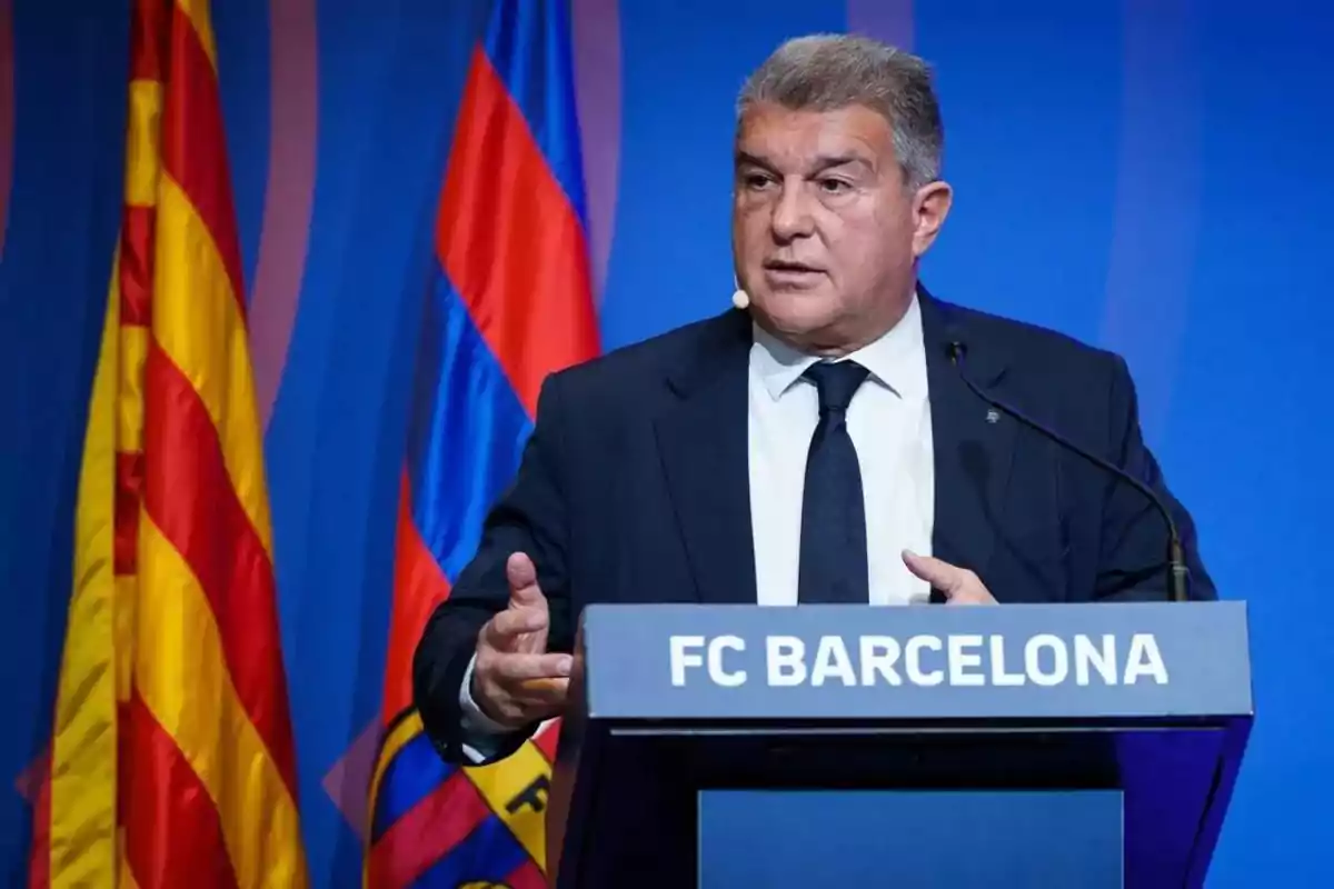 Hombre de traje y corbata hablando en un podio con el logo de FC Barcelona, con banderas en el fondo.