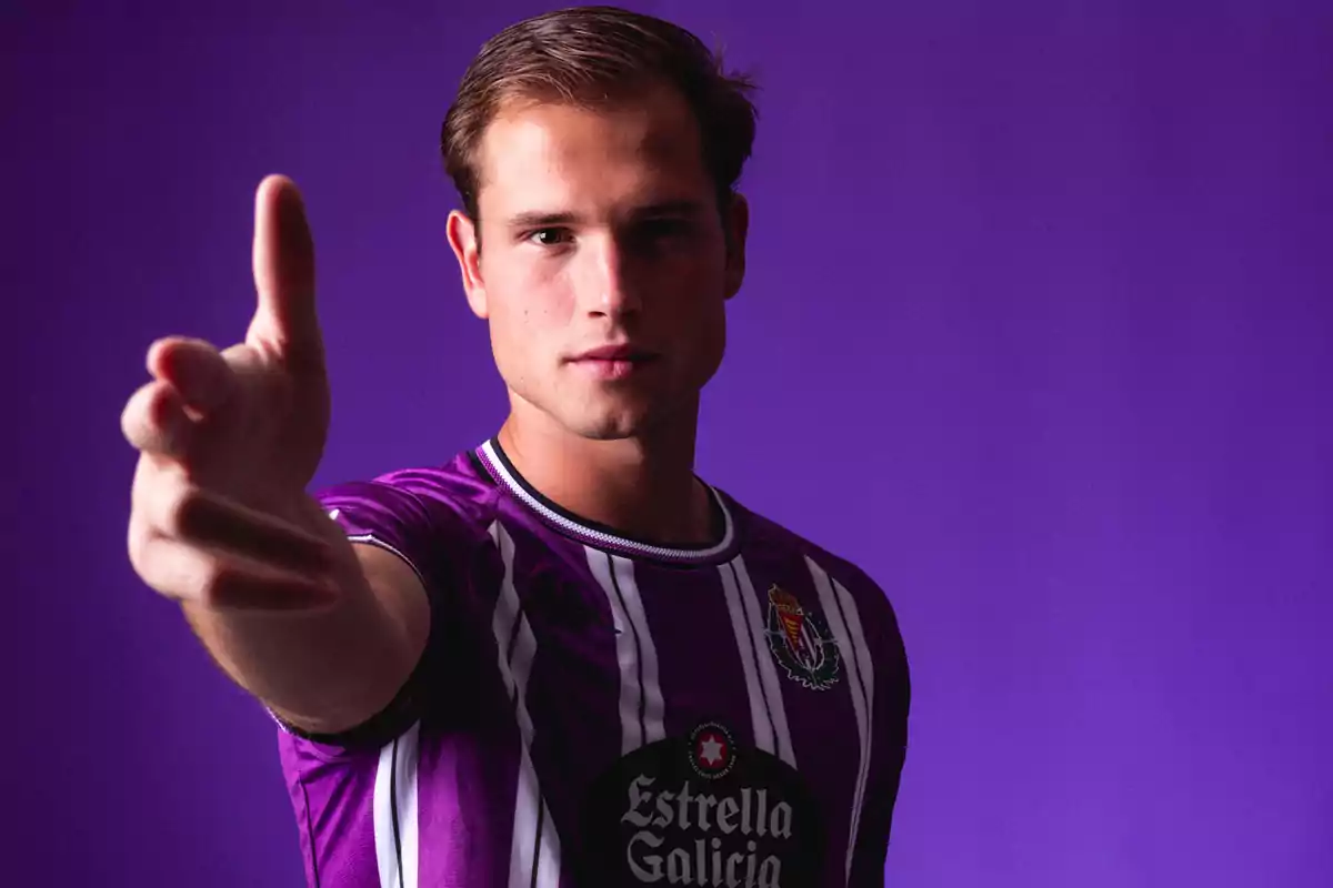 Un hombre con una camiseta morada de rayas blancas extiende su mano hacia la cámara sobre un fondo del mismo color. Un hombre con una camiseta morada de rayas blancas extiende su mano hacia la cámara sobre un fondo del mismo color.