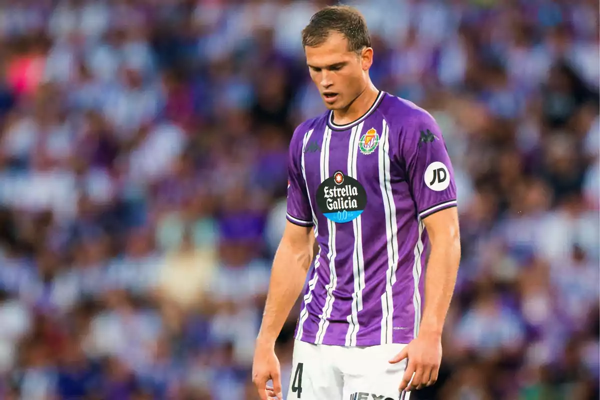 Un jugador de fútbol con uniforme morado y blanco en el campo.