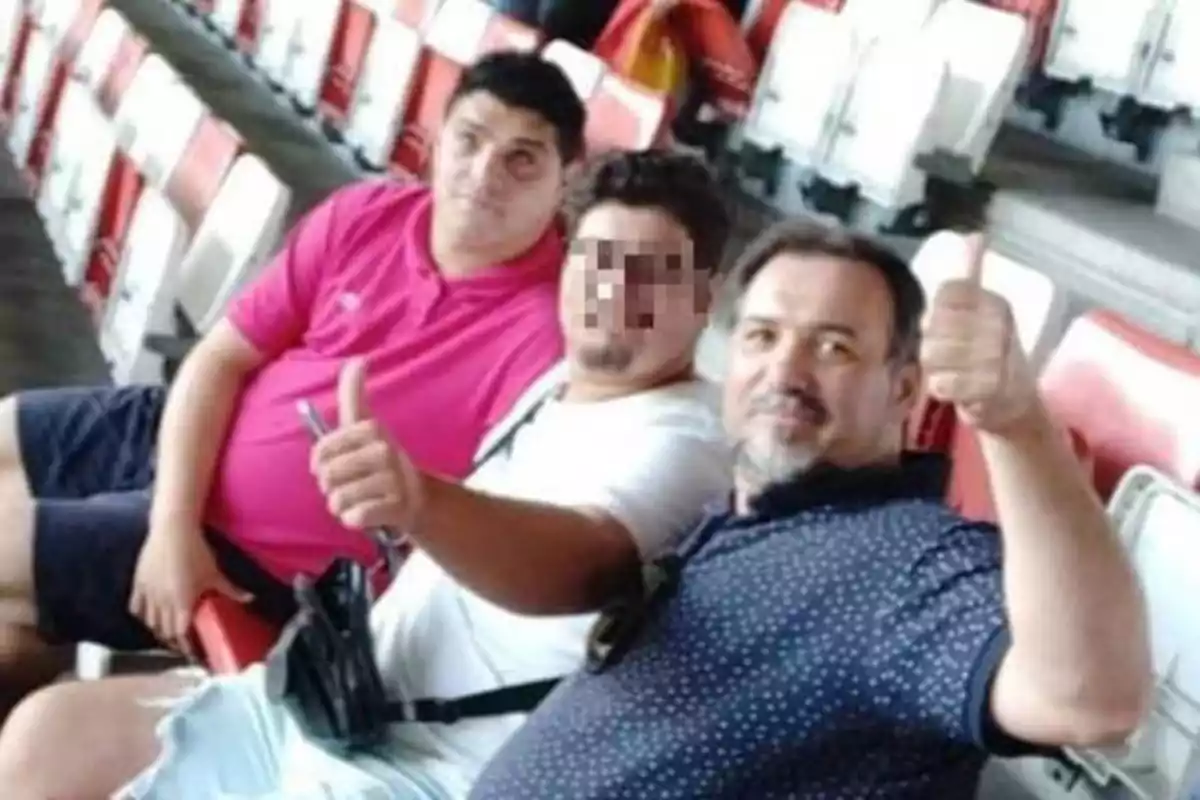 Tres hombres sentados en las gradas de un estadio, dos de ellos levantando el pulgar en señal de aprobación.