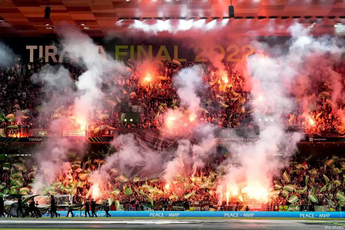 Aficionados en un estadio celebran con bengalas y humo durante un evento deportivo con un cartel que dice "Tirana Final 2022" en el fondo.