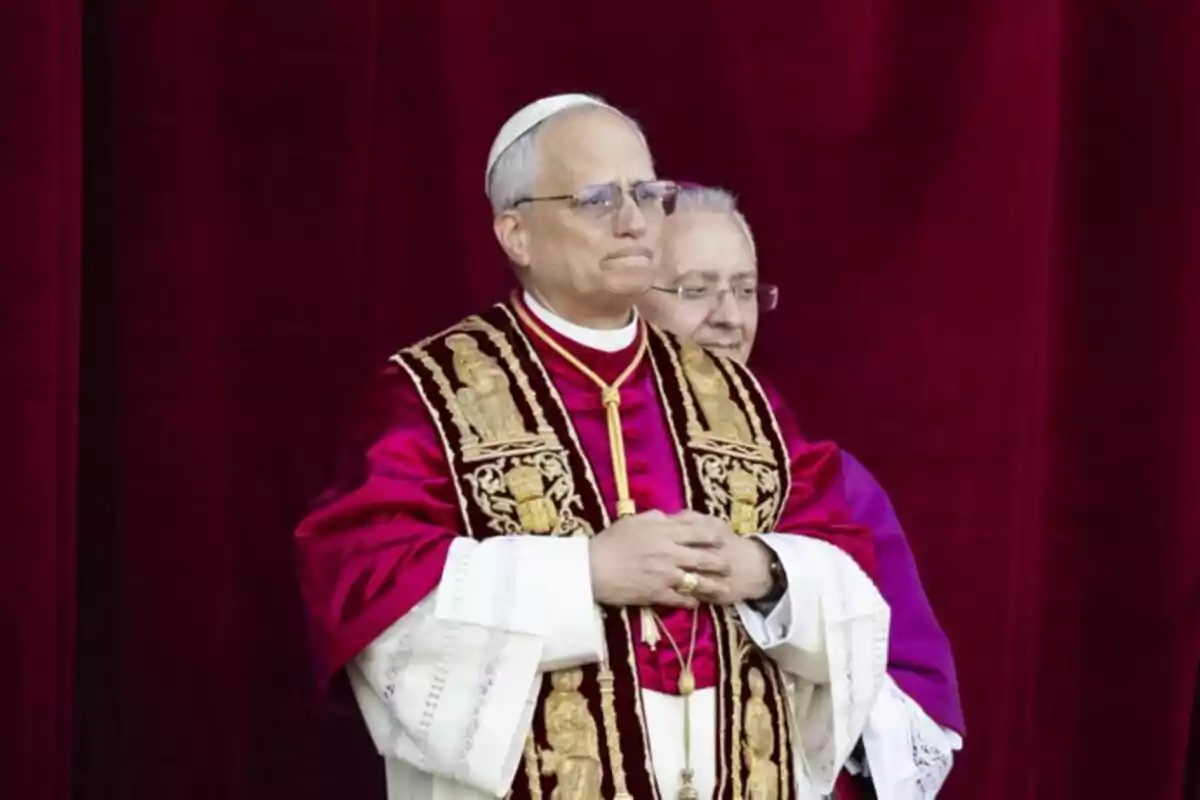 Un hombre vestido con vestimenta religiosa elaborada, incluyendo una sotana blanca y una capa bordada, está de pie frente a un fondo rojo. Un hombre vestido con vestimenta religiosa elaborada, incluyendo una sotana blanca y una capa bordada, está de pie frente a un fondo rojo.