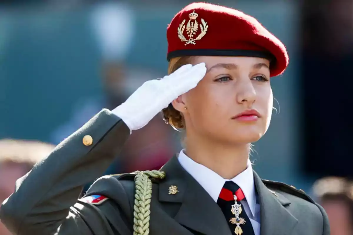 Mujer en uniforme militar saludando con una boina roja y guantes blancos.