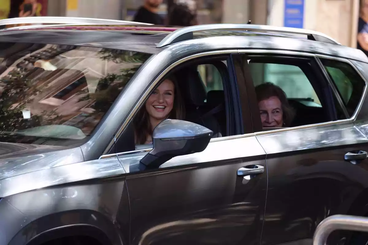 Dos personas sonrientes dentro de un automóvil plateado con las ventanas abiertas.