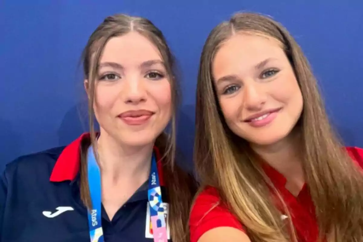 Dos jóvenes sonrientes posando para una selfie con fondo azul.