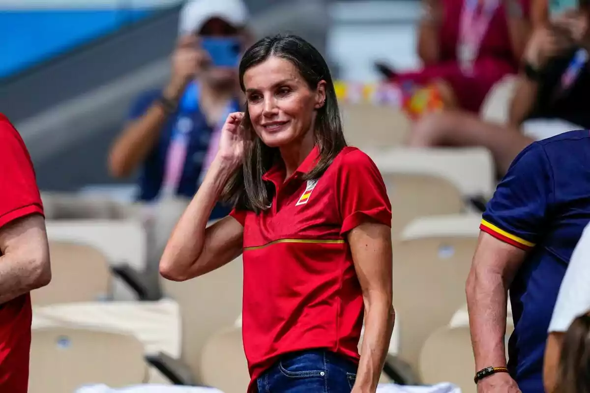 Letizia in a red t-shirt and jeans at a sporting event.