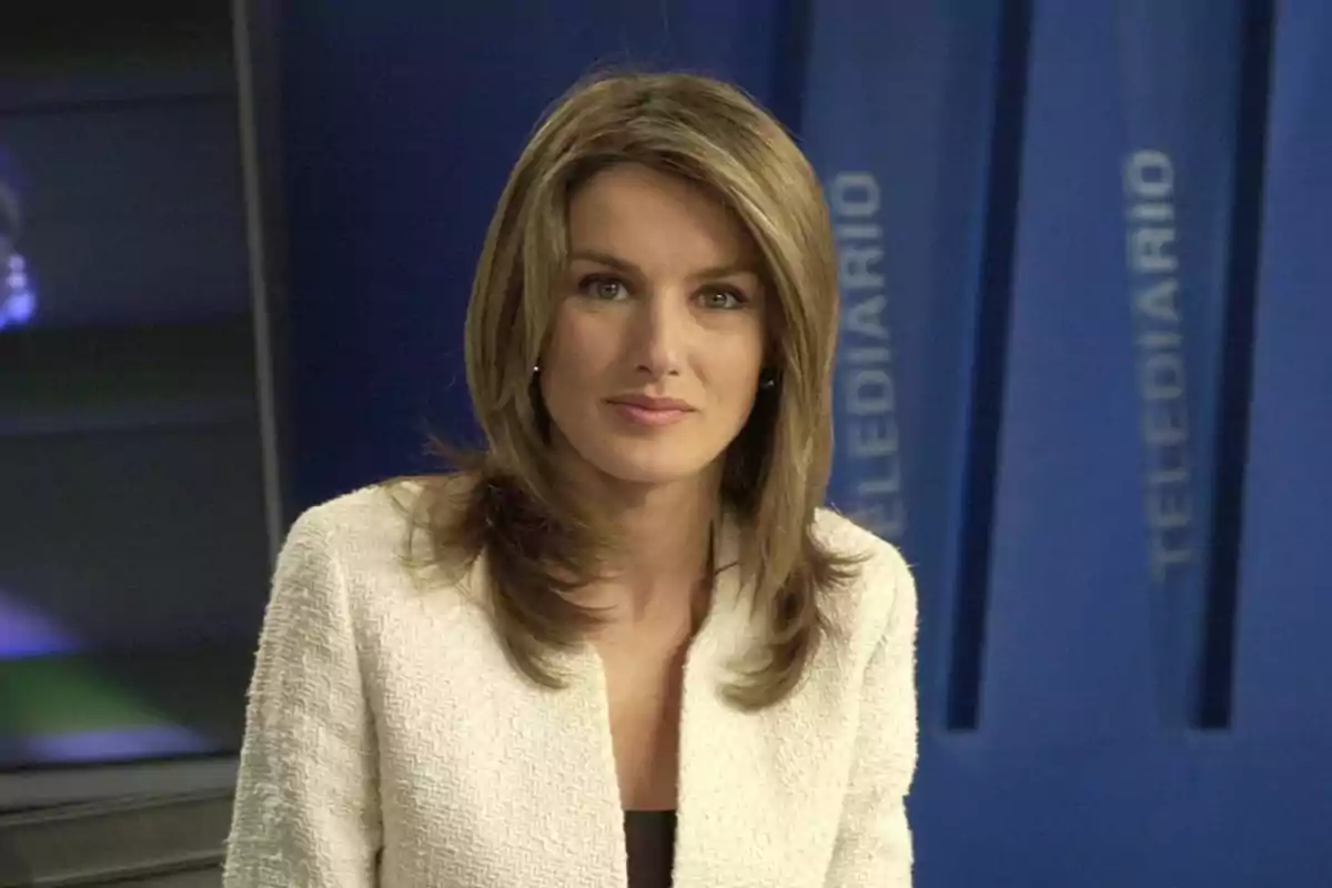 Presentadora de noticias en un estudio de televisión con fondo azul y la palabra 
