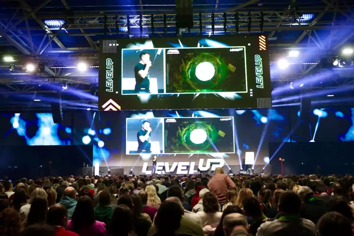 Una multitud asiste a una conferencia en un auditorio con pantallas grandes que muestran presentaciones y el texto "Level Up".