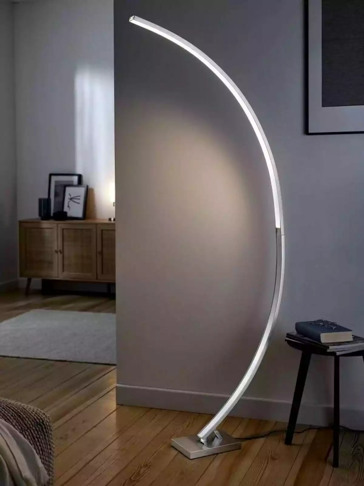 Lámpara de pie moderna con diseño curvo encendida junto a una mesa pequeña con libros en una habitación de estilo minimalista Lámpara de pie moderna con diseño curvo encendida junto a una mesa pequeña con libros en una habitación de estilo minimalista