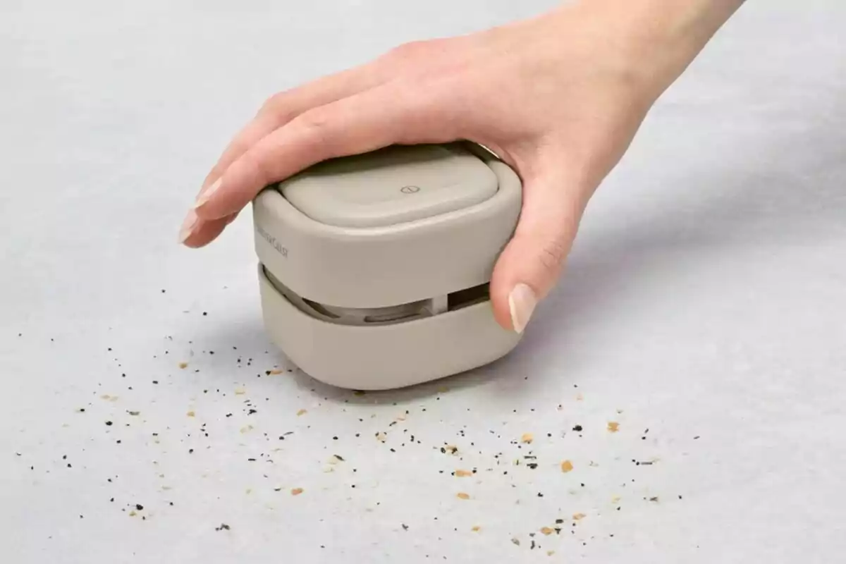 Una mano usando un pequeño aspirador portátil para recoger migas sobre una superficie clara. Una mano usando un pequeño aspirador portátil para recoger migas sobre una superficie clara.