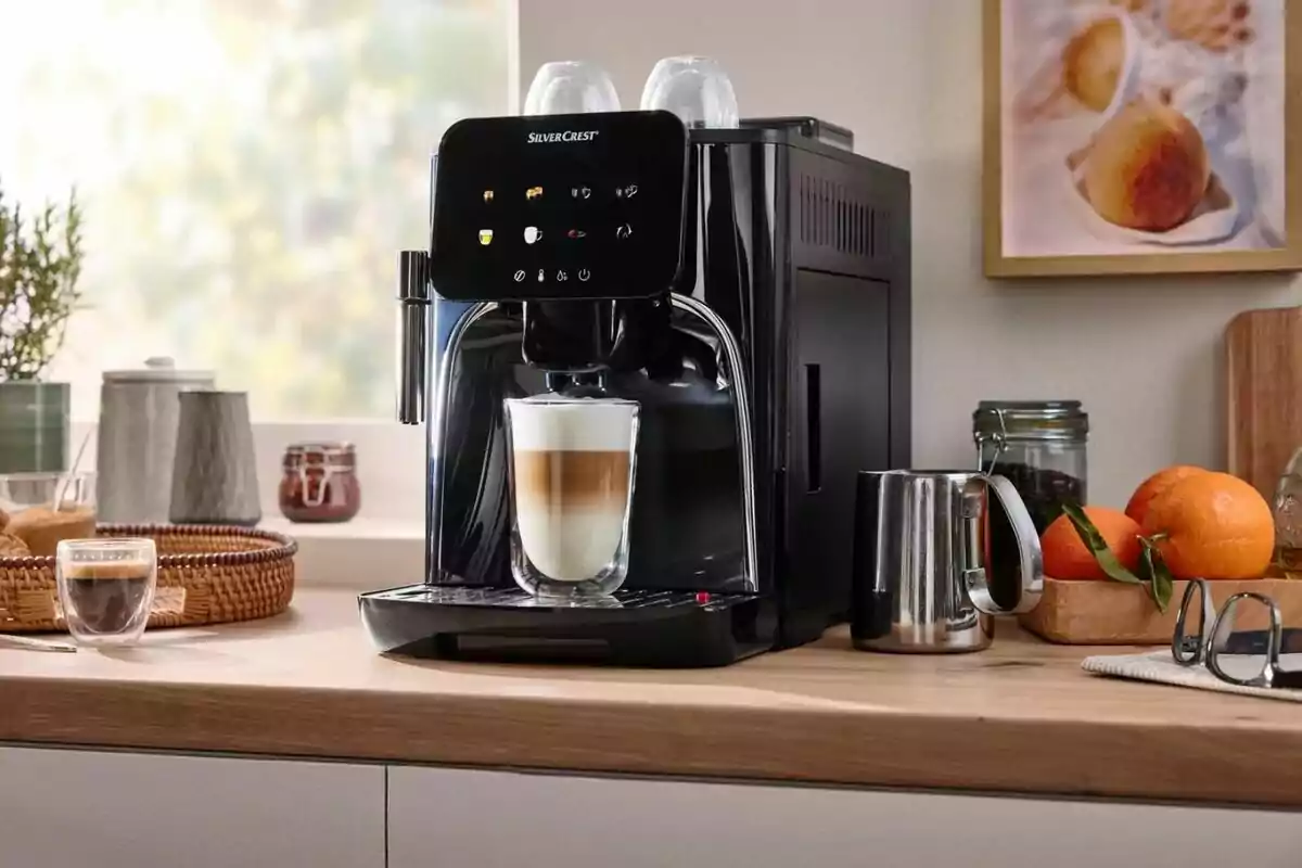 Cafetera automática negra preparando un café con leche en una cocina iluminada, rodeada de utensilios, frutas y una taza de espresso Cafetera automática negra preparando un café con leche en una cocina iluminada, rodeada de utensilios, frutas y una taza de espresso