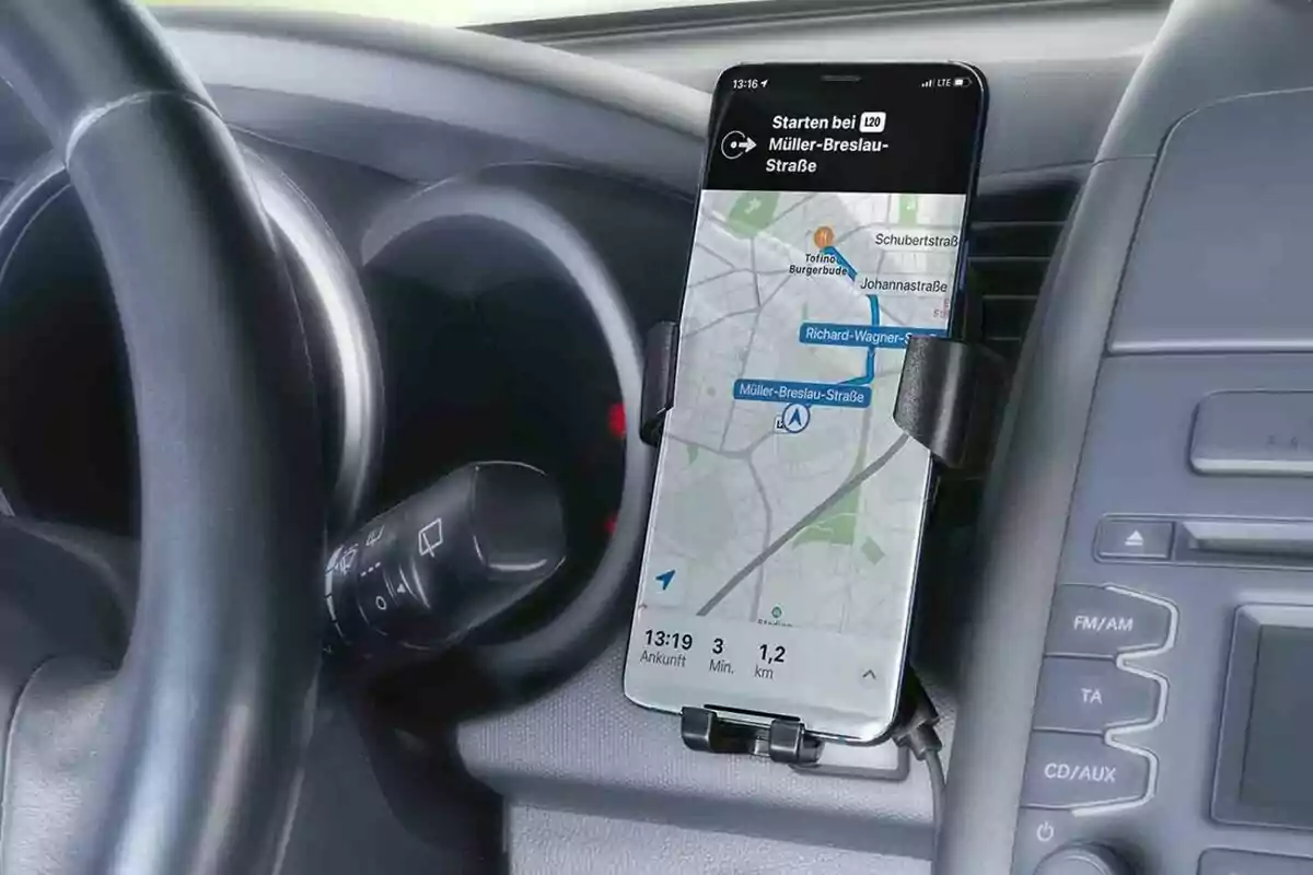Un teléfono móvil con una aplicación de navegación GPS está montado en el tablero de un automóvil junto al volante. Un teléfono móvil con una aplicación de navegación GPS está montado en el tablero de un automóvil junto al volante.