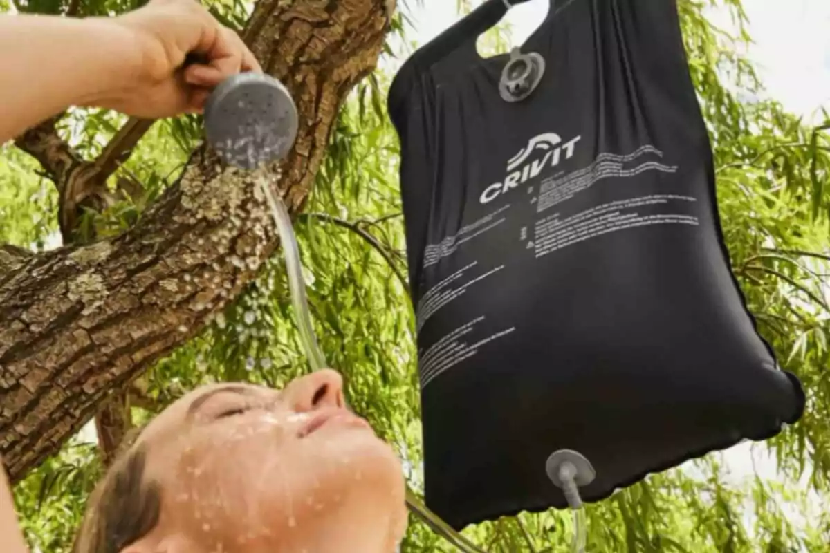 Persona disfrutando de una ducha al aire libre con una bolsa de agua colgada de un árbol. Persona disfrutando de una ducha al aire libre con una bolsa de agua colgada de un árbol.