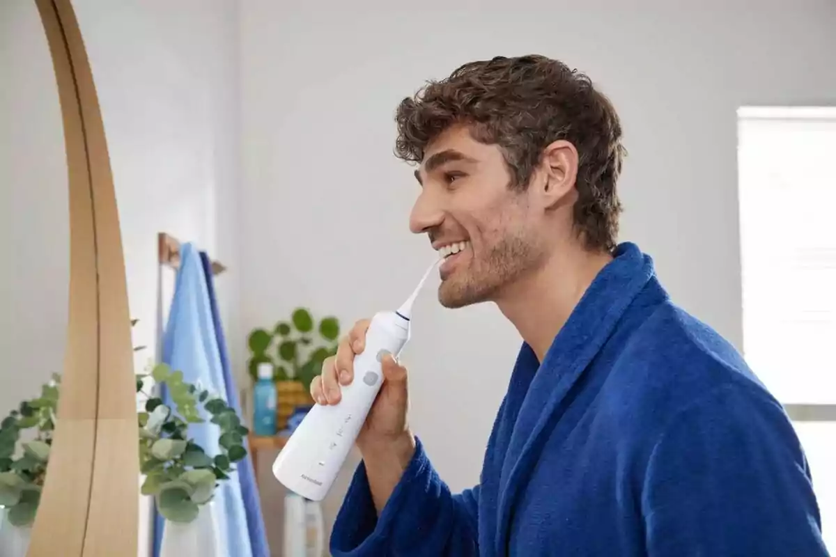 Hombre usando un irrigador dental en el baño mientras viste una bata azul. Hombre usando un irrigador dental en el baño mientras viste una bata azul.