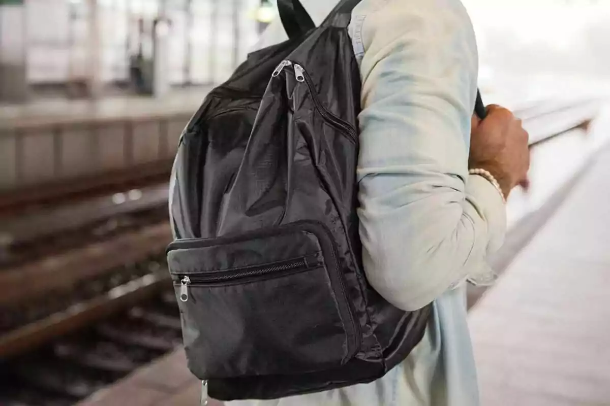 Persona con camisa clara usando una mochila negra en una estación de tren Persona con camisa clara usando una mochila negra en una estación de tren