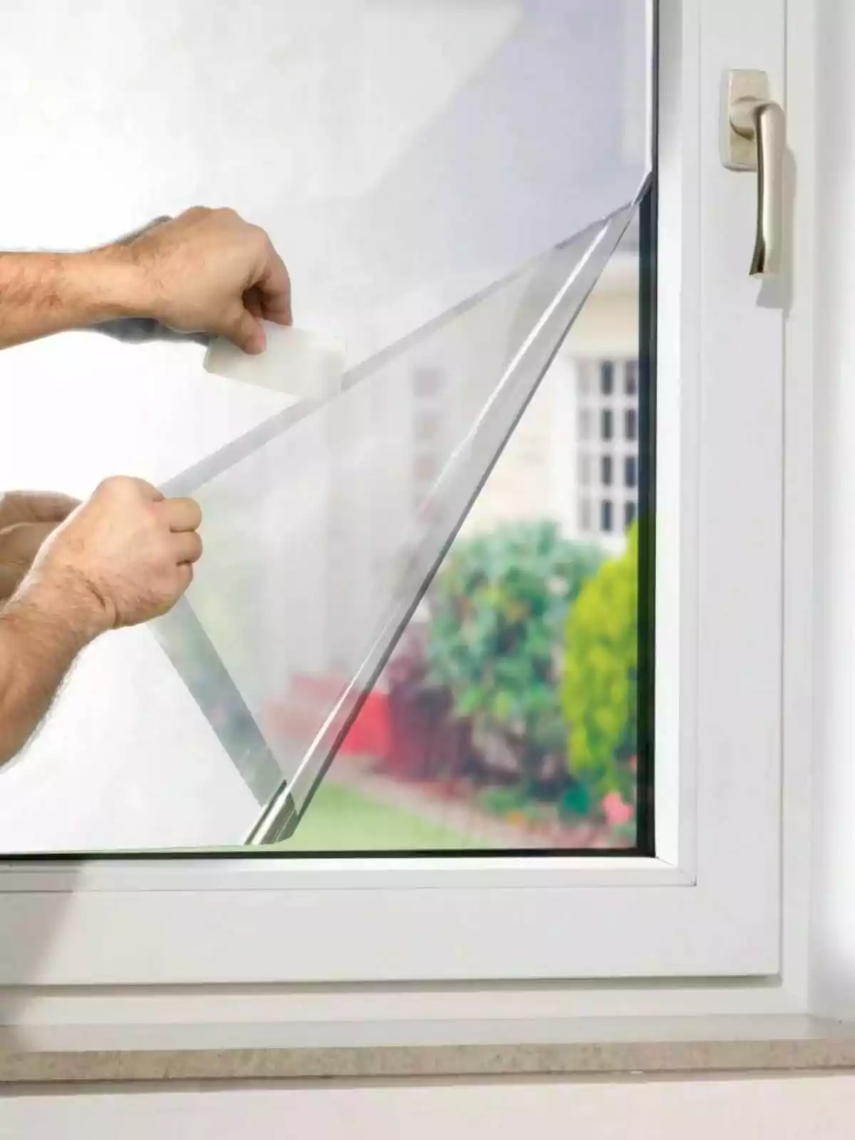 Persona instalando una lámina protectora transparente en una ventana blanca Persona instalando una lámina protectora transparente en una ventana blanca