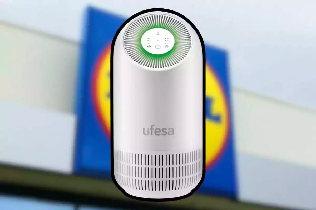 Un purificador de aire blanco de la marca Ufesa con un diseño cilíndrico y un panel de control en la parte superior, frente a un fondo desenfocado de un cartel de supermercado. Un purificador de aire blanco de la marca Ufesa con un diseño cilíndrico y un panel de control en la parte superior, frente a un fondo desenfocado de un cartel de supermercado.