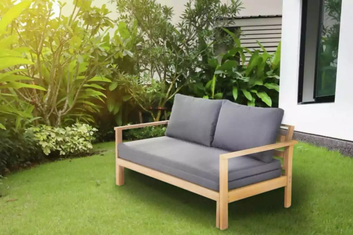Un sofá de madera con cojines grises en un jardín verde y soleado. Un sofá de madera con cojines grises en un jardín verde y soleado.