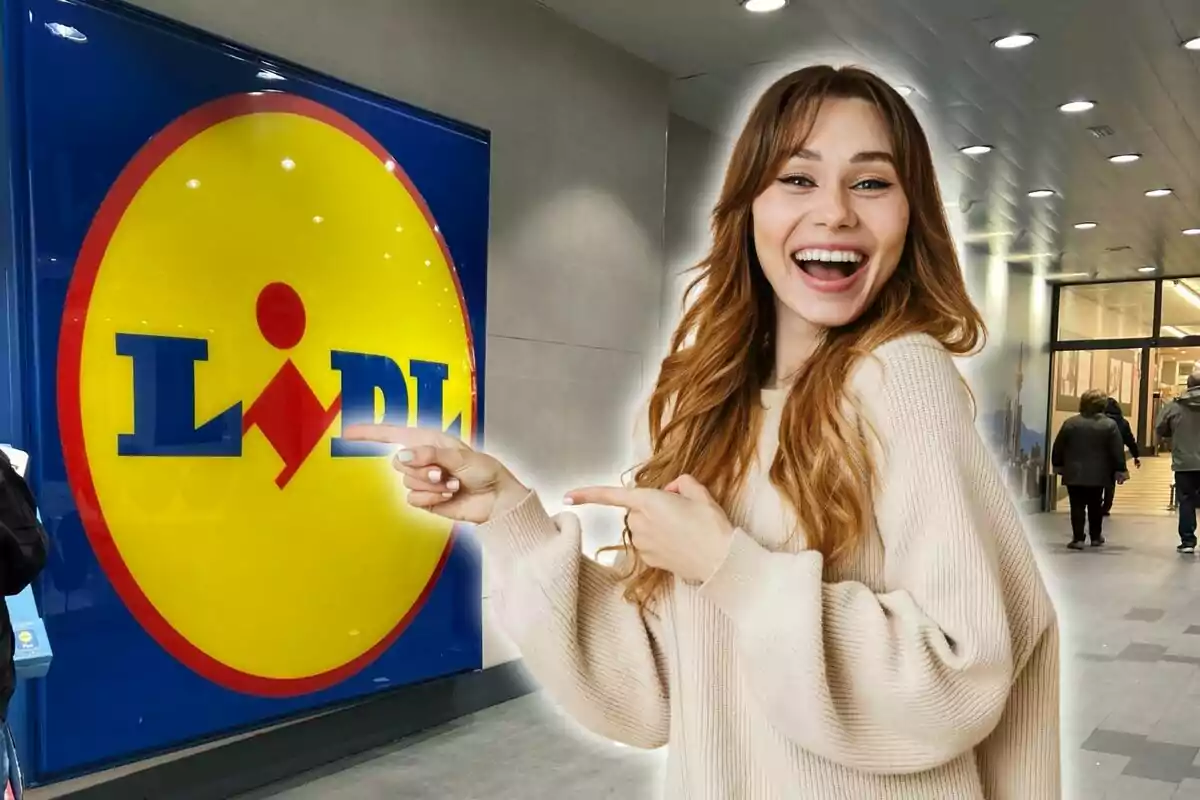 Una mujer sonriente con cabello largo y castaño claro, vestida con un suéter beige, señala con ambas manos el logotipo de Lidl en la entrada de una tienda.