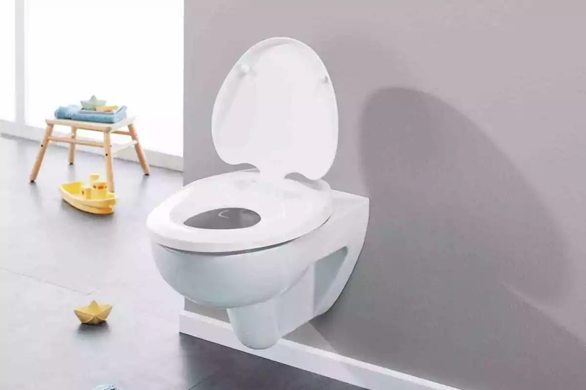 Inodoro blanco montado en la pared con tapa abierta en un baño infantil, con juguetes y una silla pequeña en el fondo. Inodoro blanco montado en la pared con tapa abierta en un baño infantil, con juguetes y una silla pequeña en el fondo.
