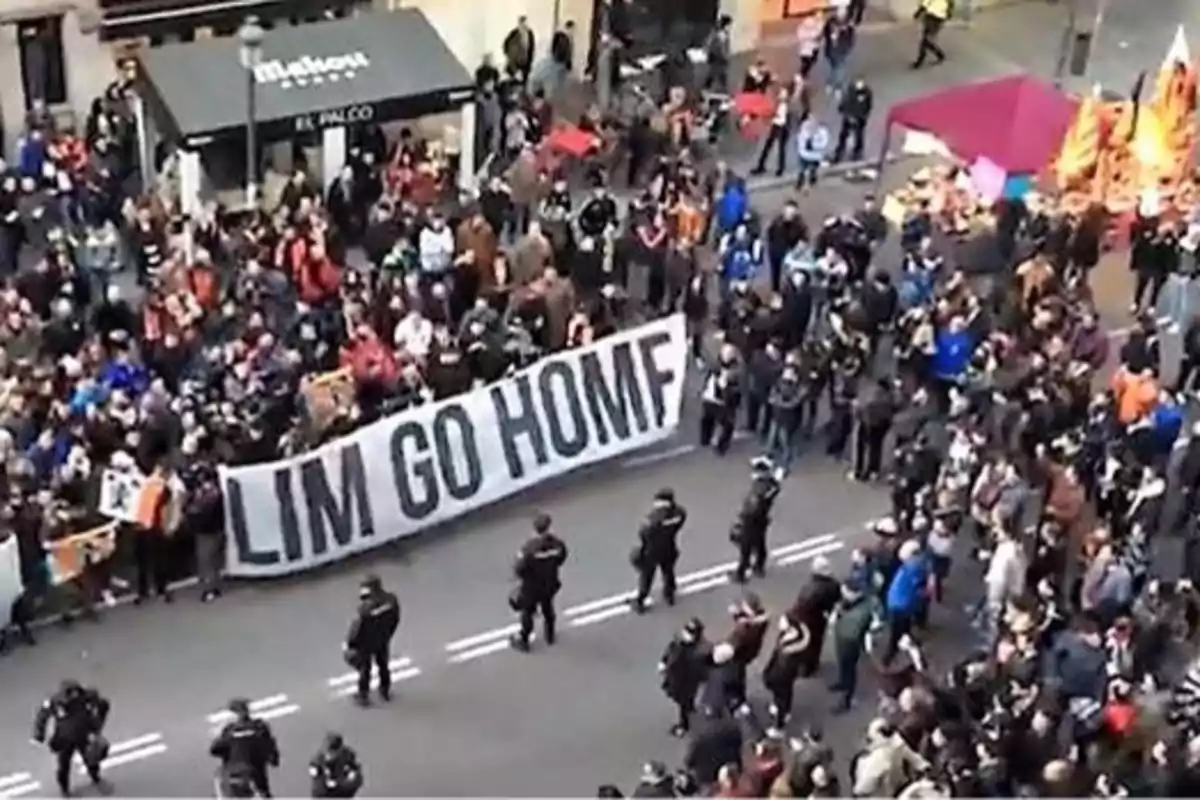 Una multitud de personas se reúne en una calle, sosteniendo una pancarta grande que dice 