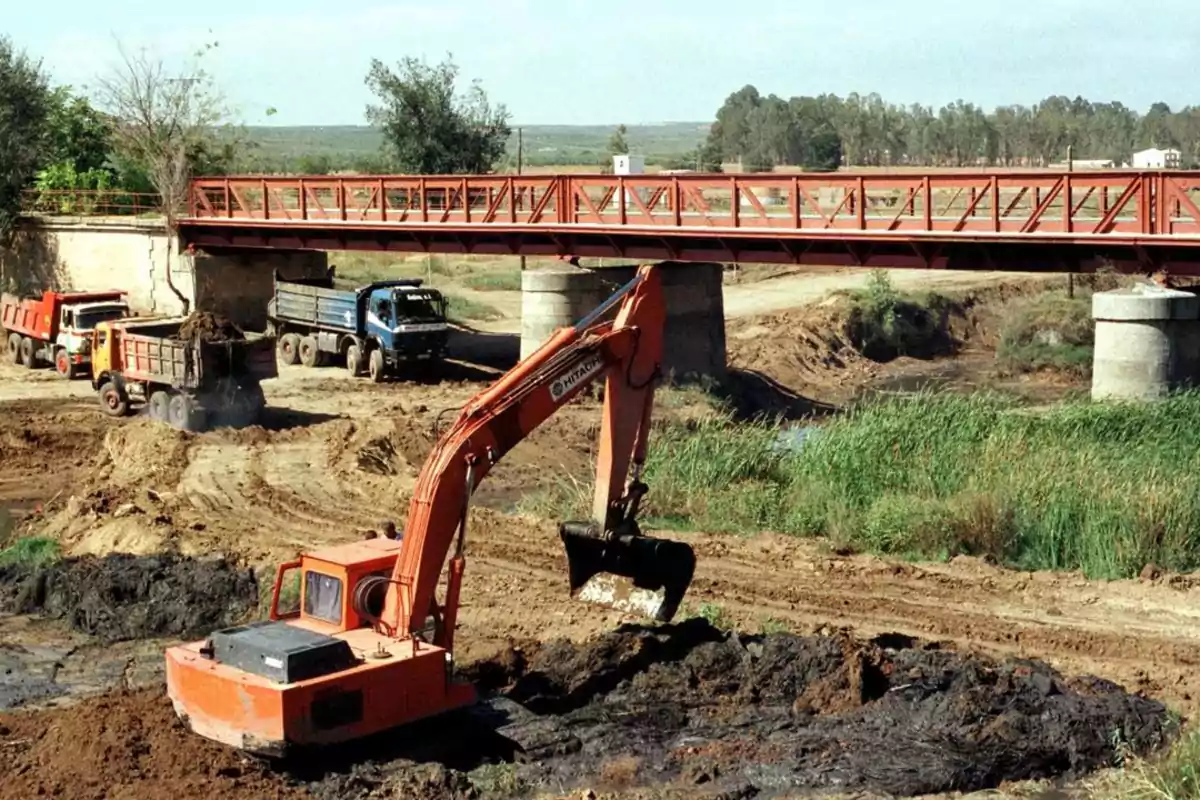 Excavadora y camiones trabajando en la construcción de un puente.