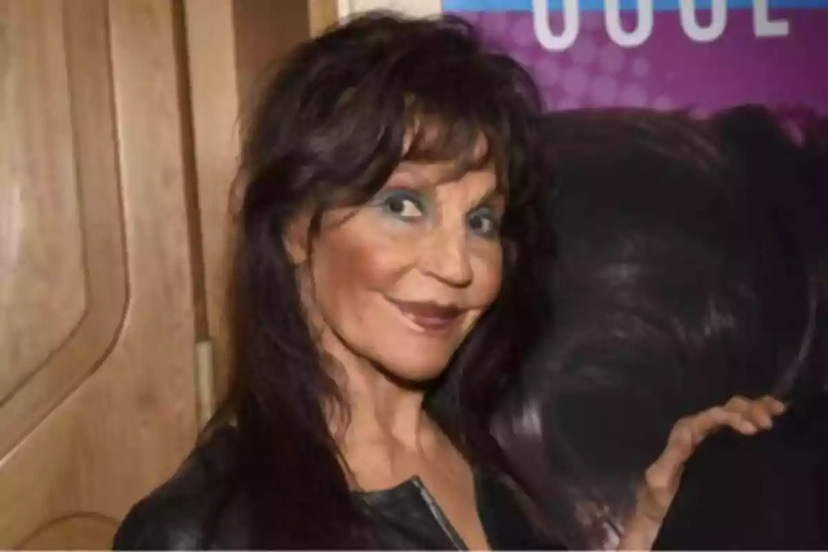 Mujer de cabello oscuro y largo con maquillaje llamativo sonriendo y posando frente a un fondo colorido Mujer de cabello oscuro y largo con maquillaje llamativo sonriendo y posando frente a un fondo colorido