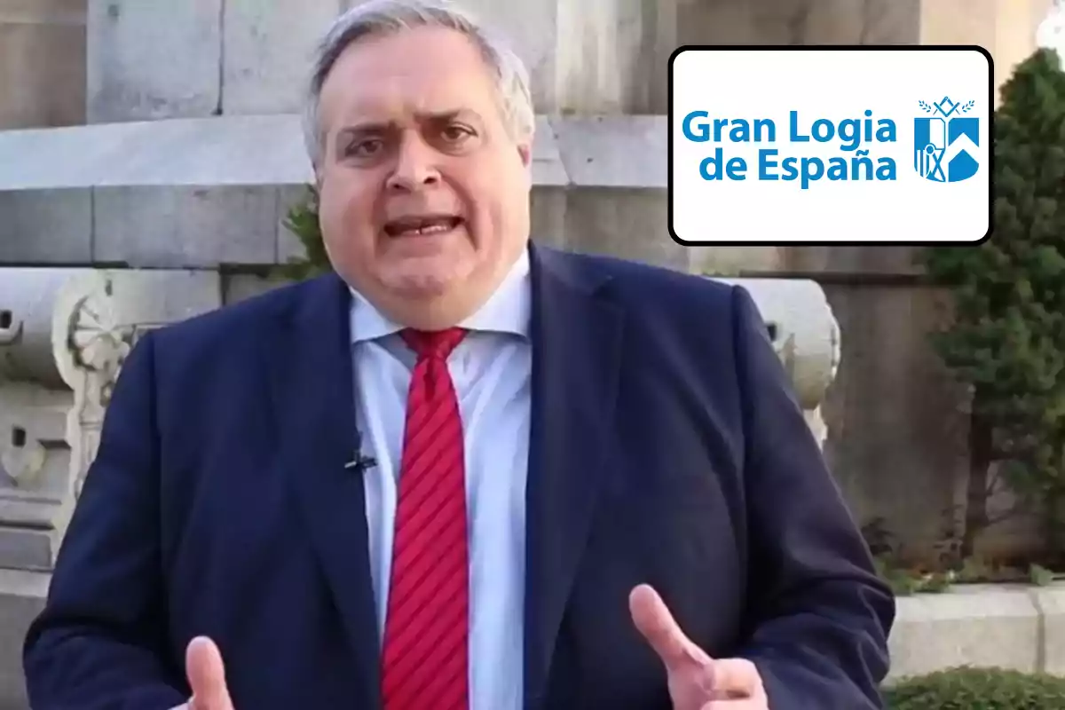 Un hombre con traje y corbata roja está hablando al aire libre, con un logotipo de la Gran Logia de España en la esquina superior derecha.