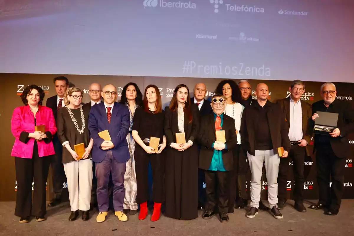 Un grupo de personas posando en un escenario durante un evento de premios, algunas sosteniendo trofeos, con un fondo que muestra logotipos de empresas patrocinadoras.