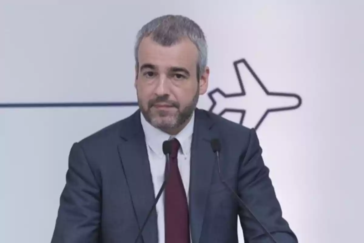 Hombre de traje hablando frente a dos micrófonos con un dibujo de avión en el fondo Hombre de traje hablando frente a dos micrófonos con un dibujo de avión en el fondo
