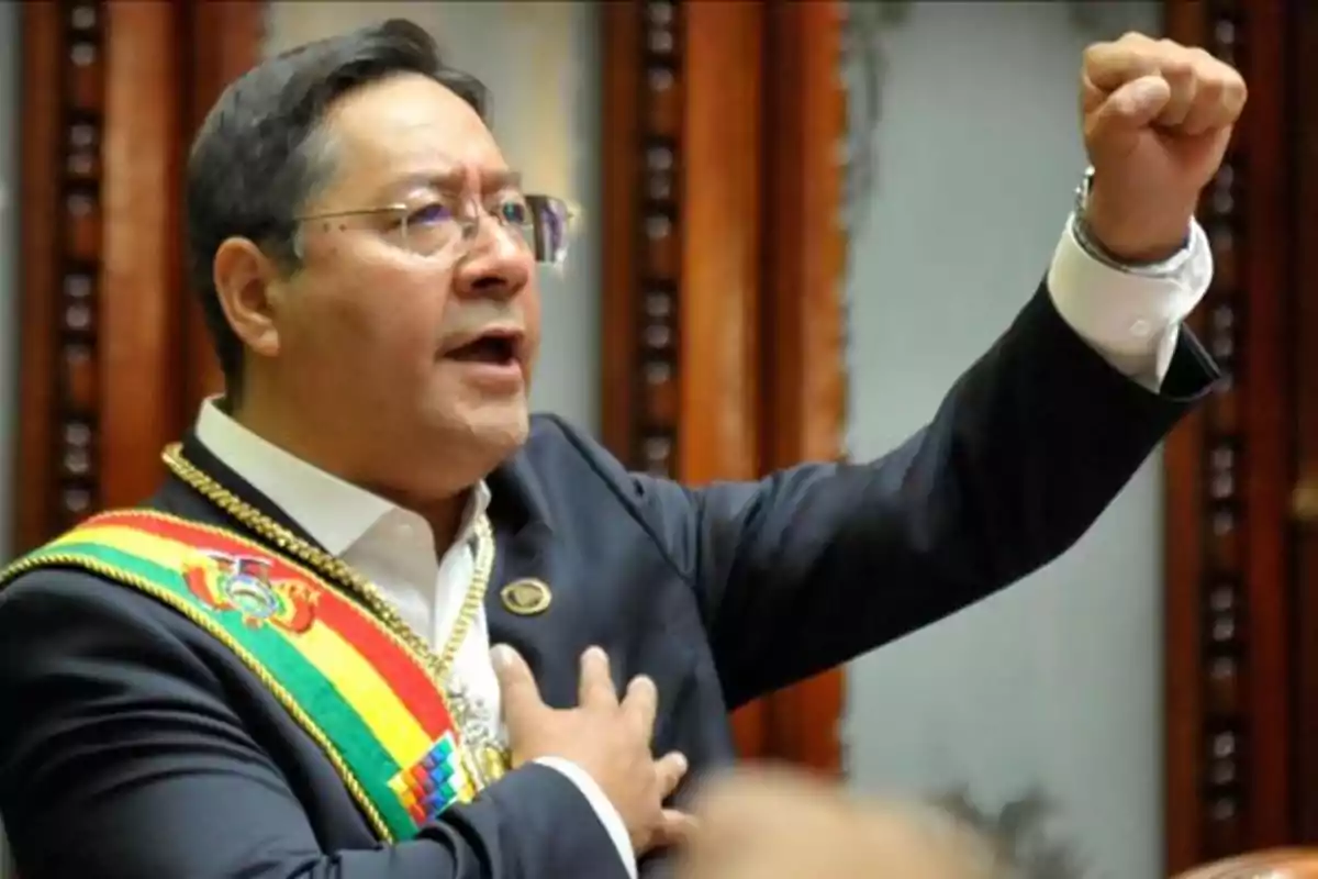Un hombre con gafas y una banda presidencial de Bolivia levanta el puño mientras habla apasionadamente.