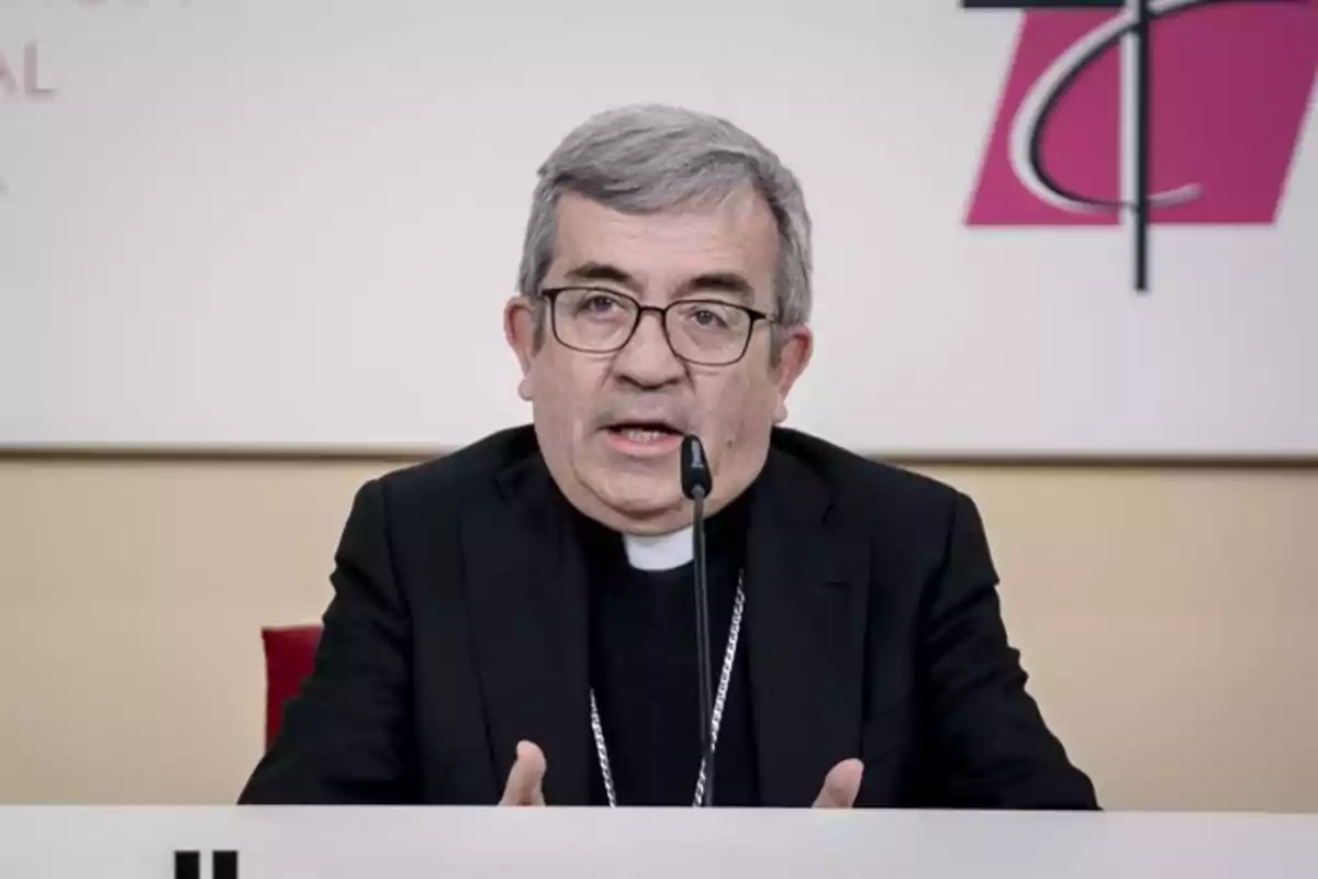 Un hombre con gafas y vestimenta clerical habla frente a un micrófono en una conferencia de prensa.