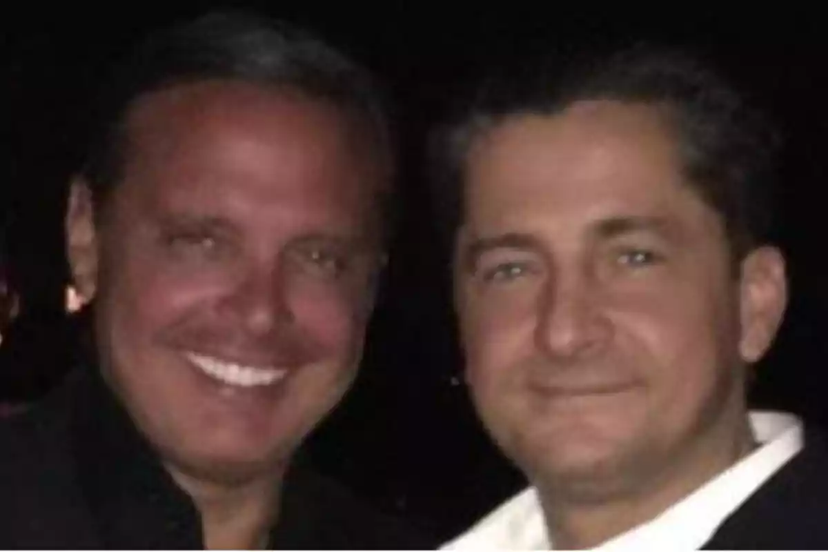 Dos hombres sonriendo en una foto tomada en un ambiente oscuro.