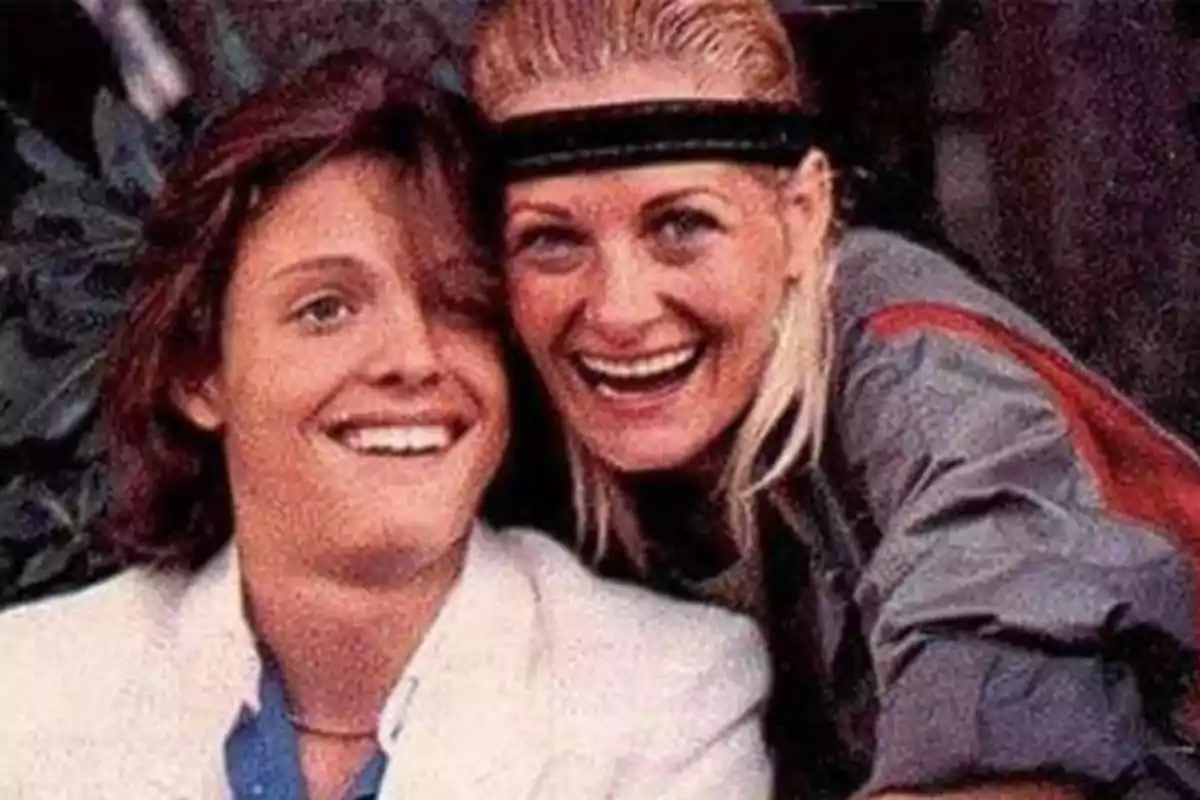 Dos personas sonrientes posando para una foto, una con cabello corto y castaño y la otra con cabello rubio y una cinta en la cabeza.