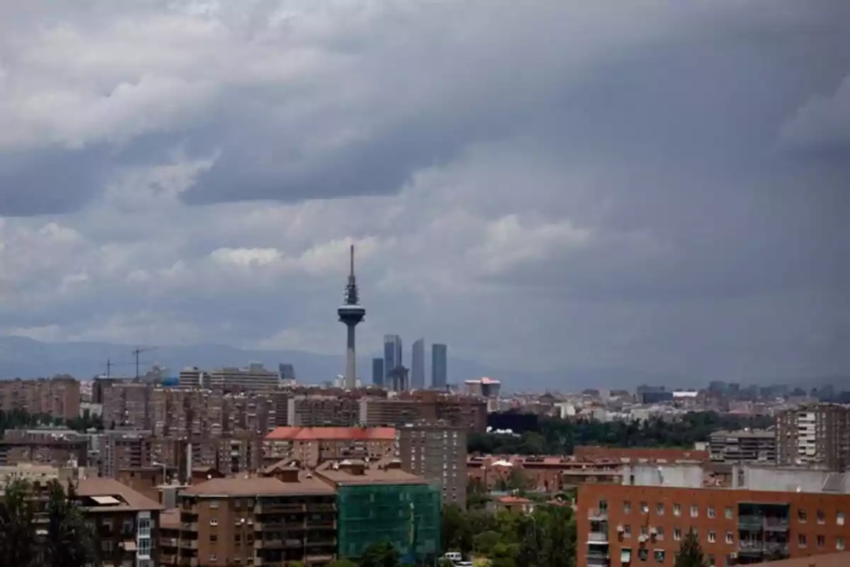 Vista panorámica de una ciudad con edificios altos y una torre de telecomunicaciones bajo un cielo nublado.