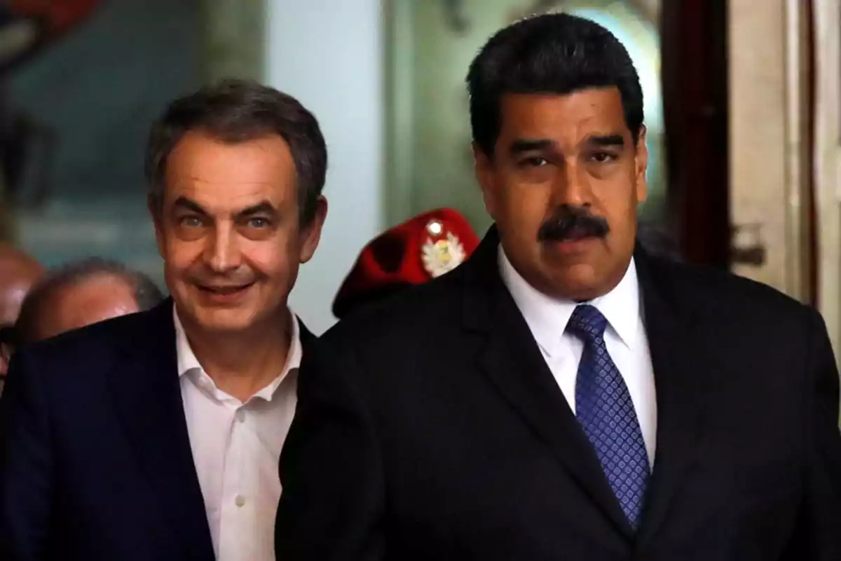 Dos hombres de traje, uno con camisa blanca y el otro con corbata azul, caminando juntos en un entorno formal.