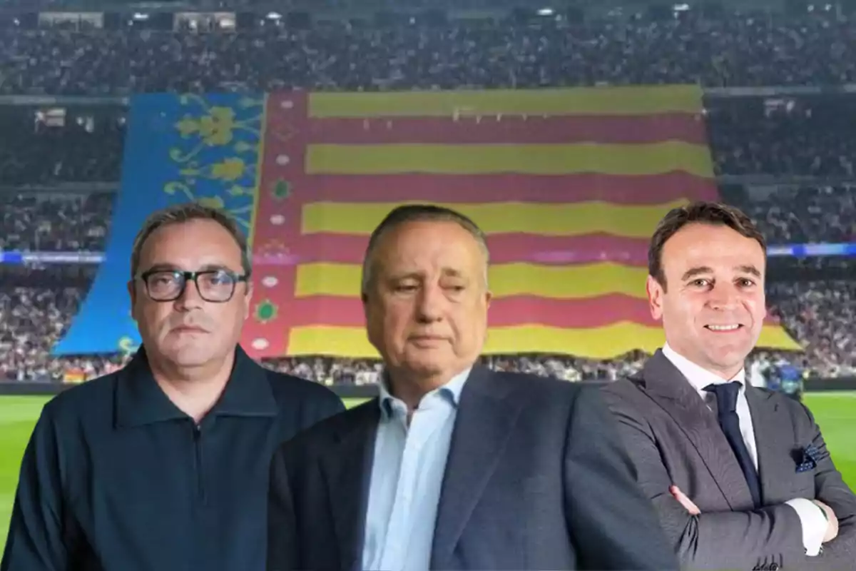 Tres hombres posan frente a una gran bandera en un estadio lleno de espectadores.