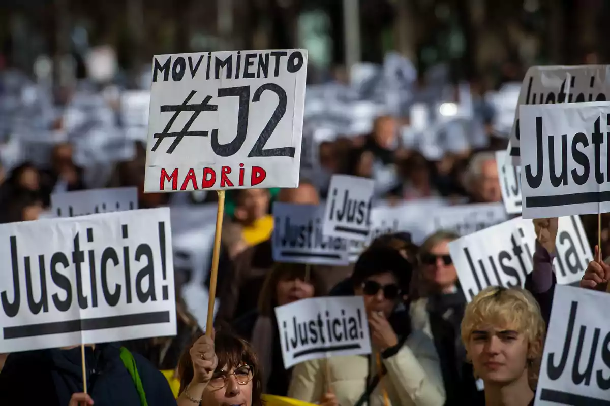 Personas en una manifestación sosteniendo carteles que piden justicia y muestran apoyo al movimiento J2 en Madrid.