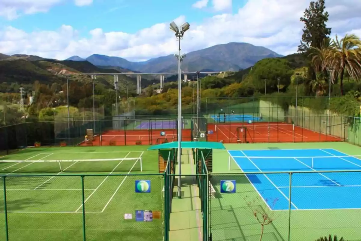 Vista de un complejo de canchas de tenis al aire libre rodeado de montañas y vegetación.