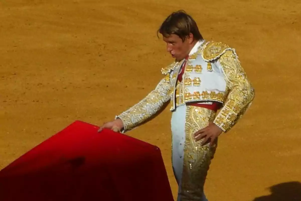 Un torero en la plaza de toros sosteniendo un capote rojo.