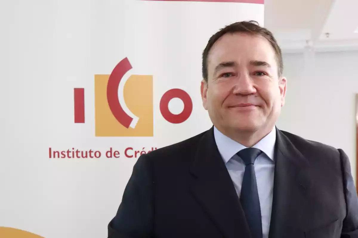 Hombre con traje oscuro y corbata azul posando frente a un cartel del Instituto de Crédito Oficial Hombre con traje oscuro y corbata azul posando frente a un cartel del Instituto de Crédito Oficial