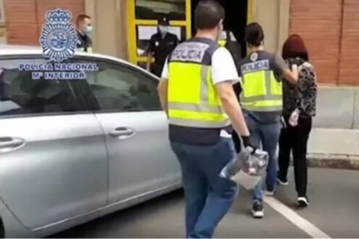 Agentes de la Policía Nacional escoltan a una persona hacia un edificio mientras llevan objetos en bolsas de evidencia.