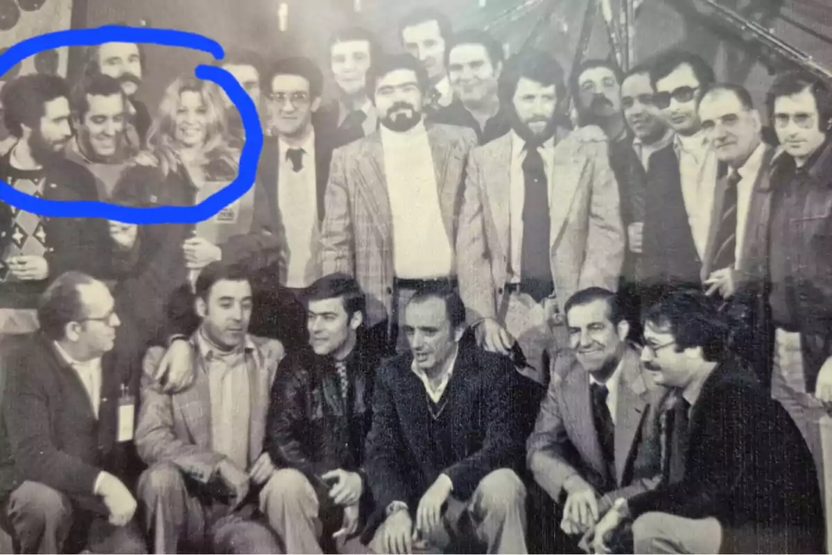Un grupo de personas posando para una foto en blanco y negro, con una mujer en el centro del grupo rodeada por un círculo azul. Un grupo de personas posando para una foto en blanco y negro, con una mujer en el centro del grupo rodeada por un círculo azul.