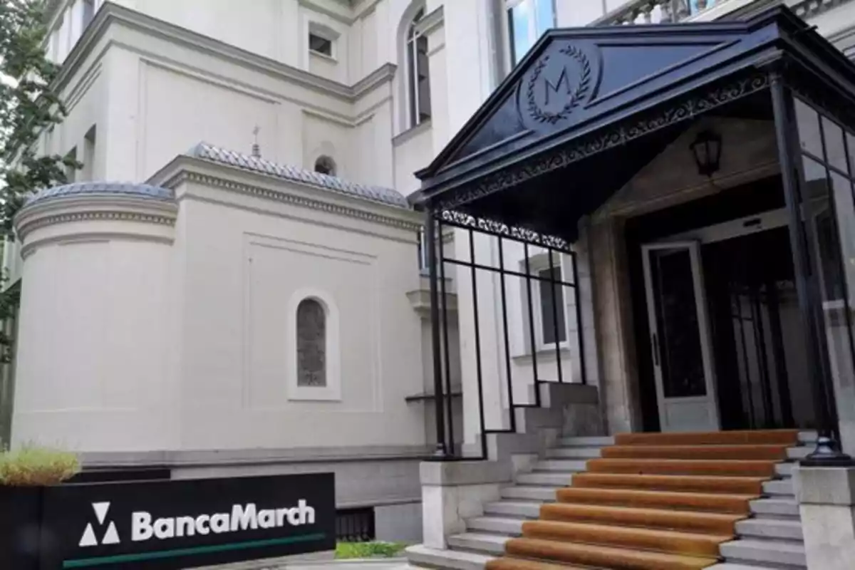 Entrada principal de un edificio elegante con escaleras alfombradas y un letrero de Banca March en la parte frontal Entrada principal de un edificio elegante con escaleras alfombradas y un letrero de Banca March en la parte frontal